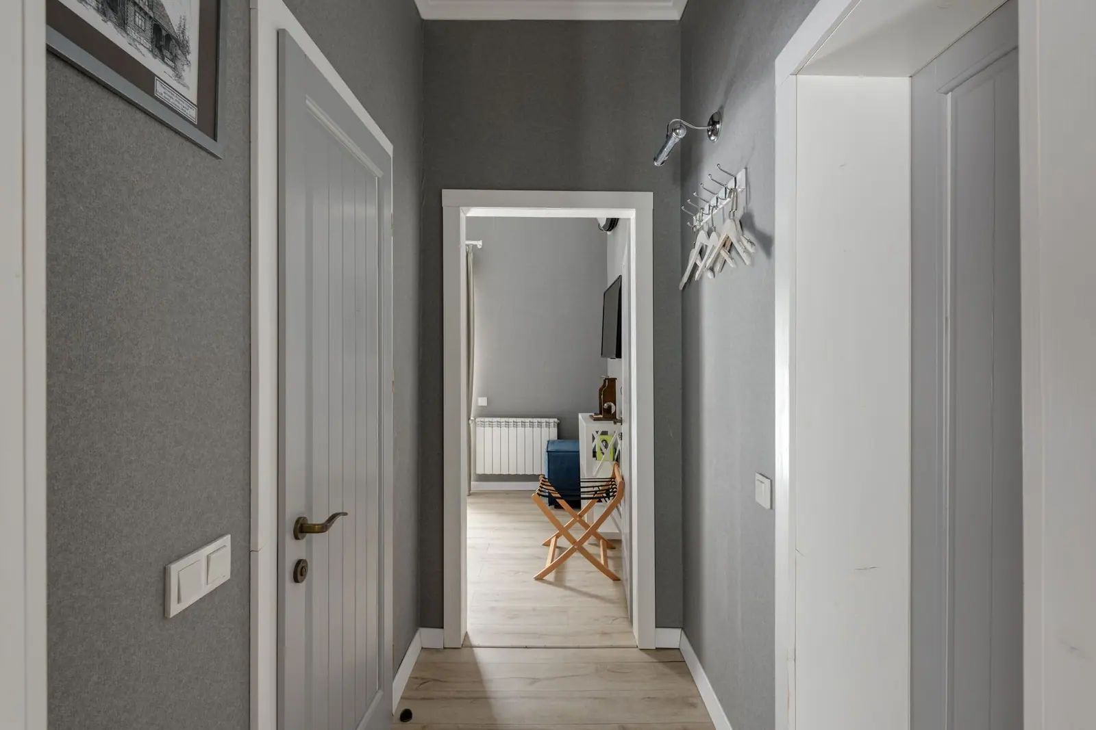 A gray hallway with an open white door and rooms beyond