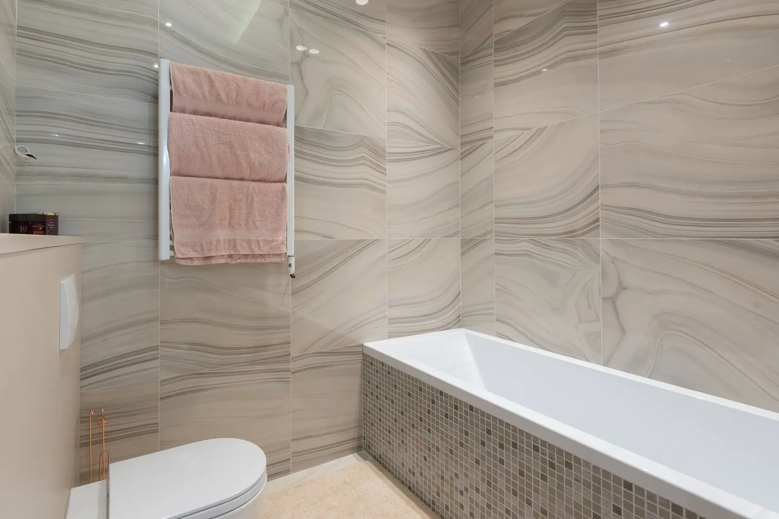 A white bathtub set against a marble-patterned wall surround