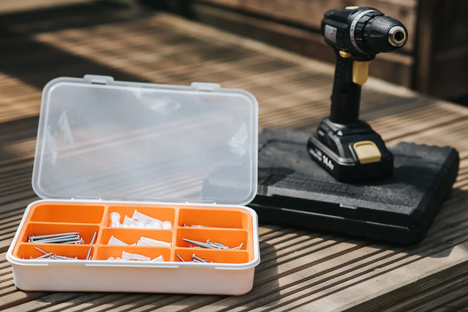 A cordless drill beside a case of screws and fixings