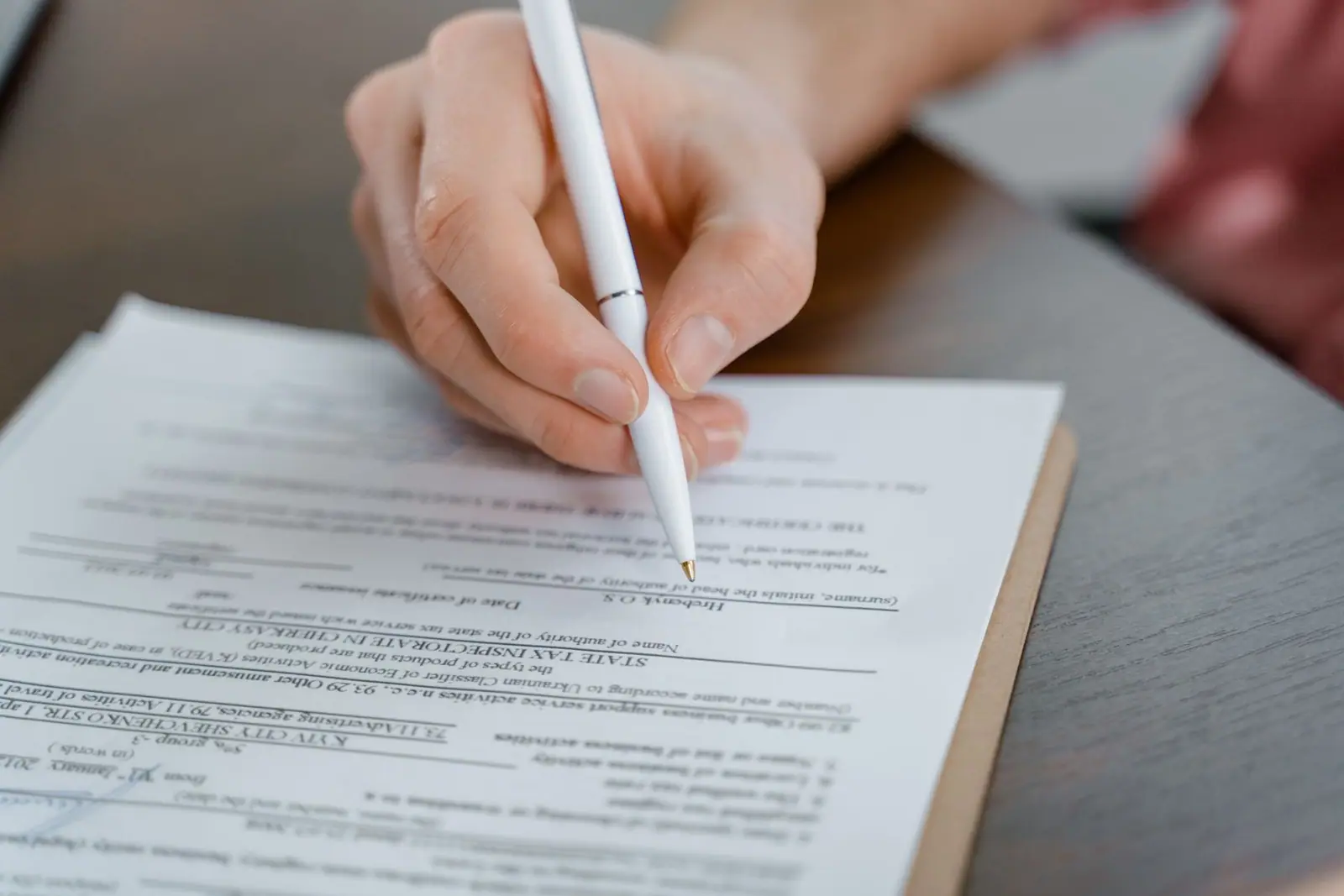 A hand signing a printed document with a pen