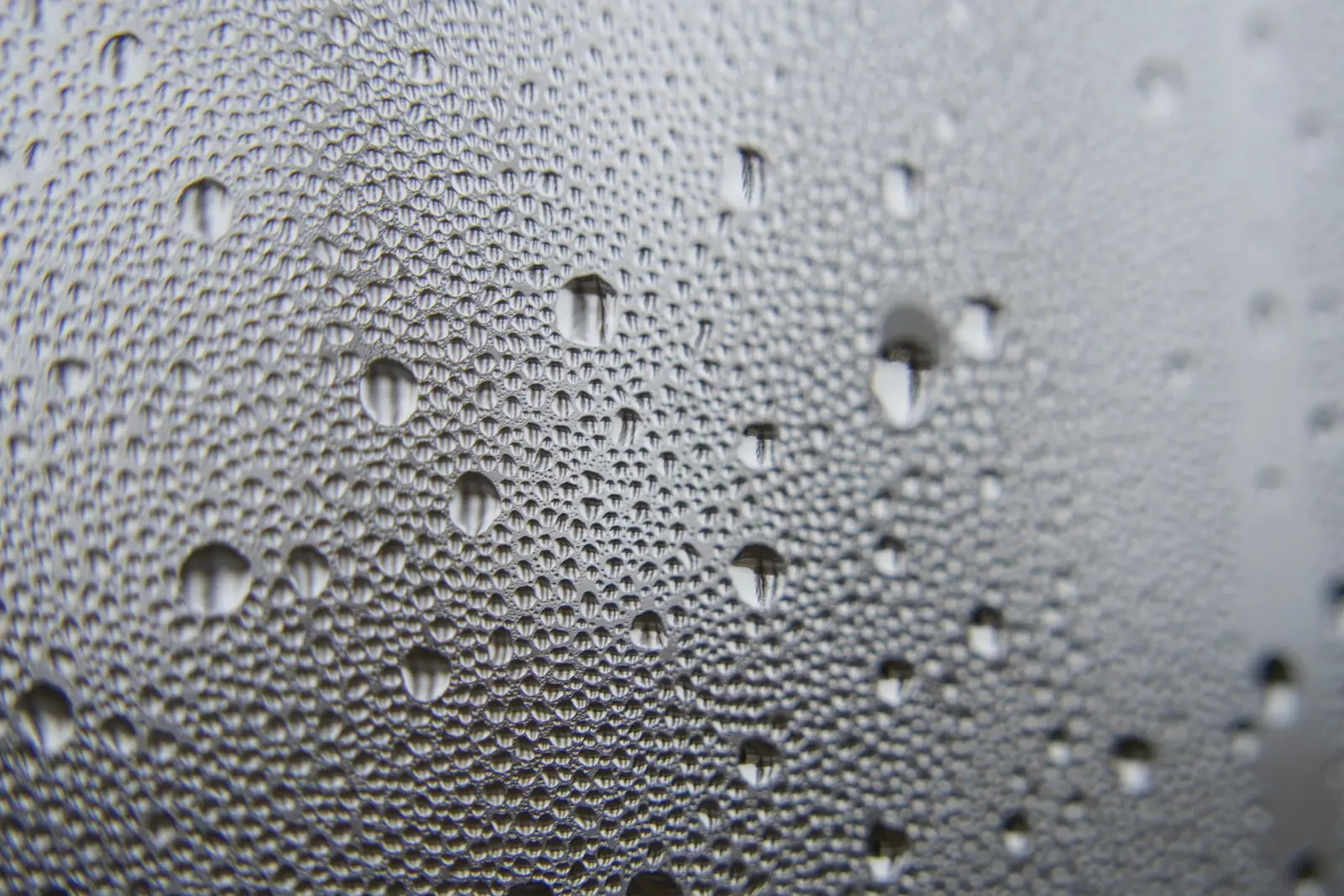 Small water droplets covering a glass surface against a gray background