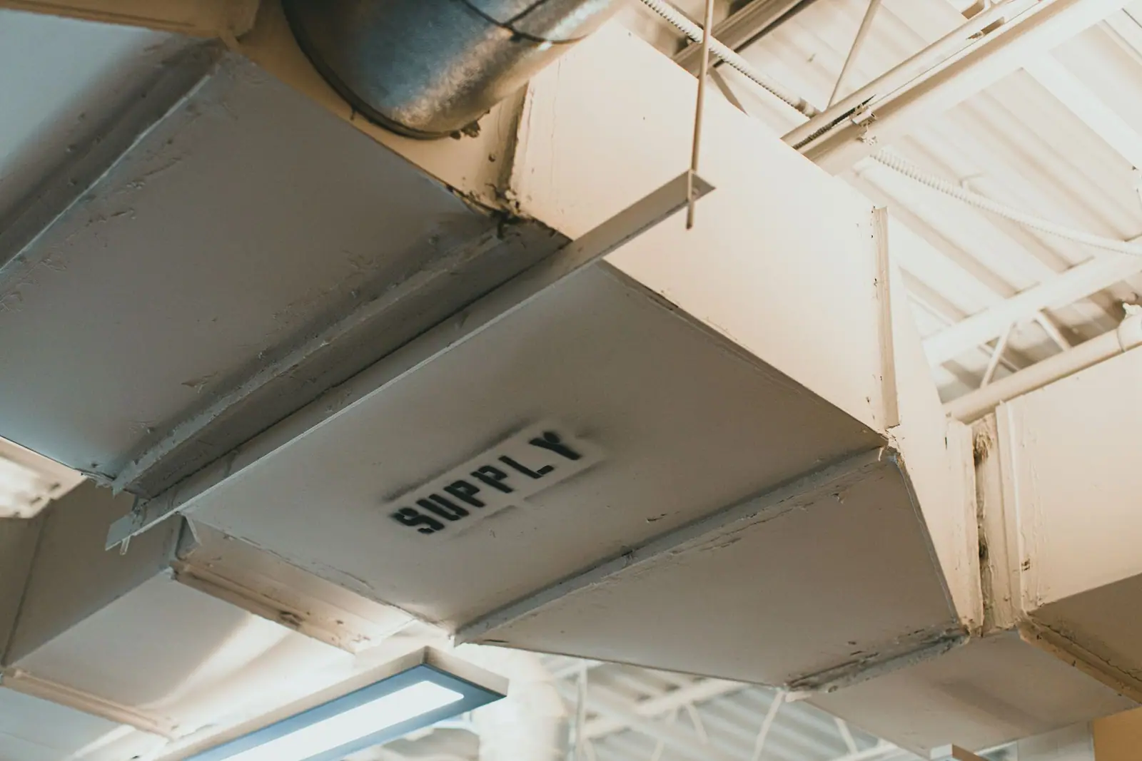 A rectangular metal duct labeled SUPPLY connected to round ductwork beneath an exposed ceiling