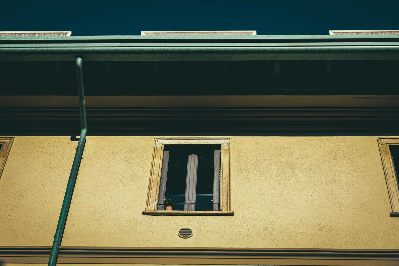 A green downspout running down the wall of a house beneath a roof gutter