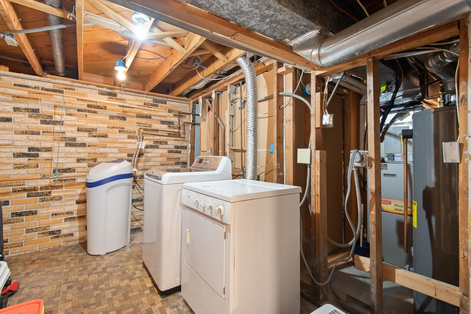 Laundry machines and a tall tank water heater in an unfinished basement with exposed ceiling framing