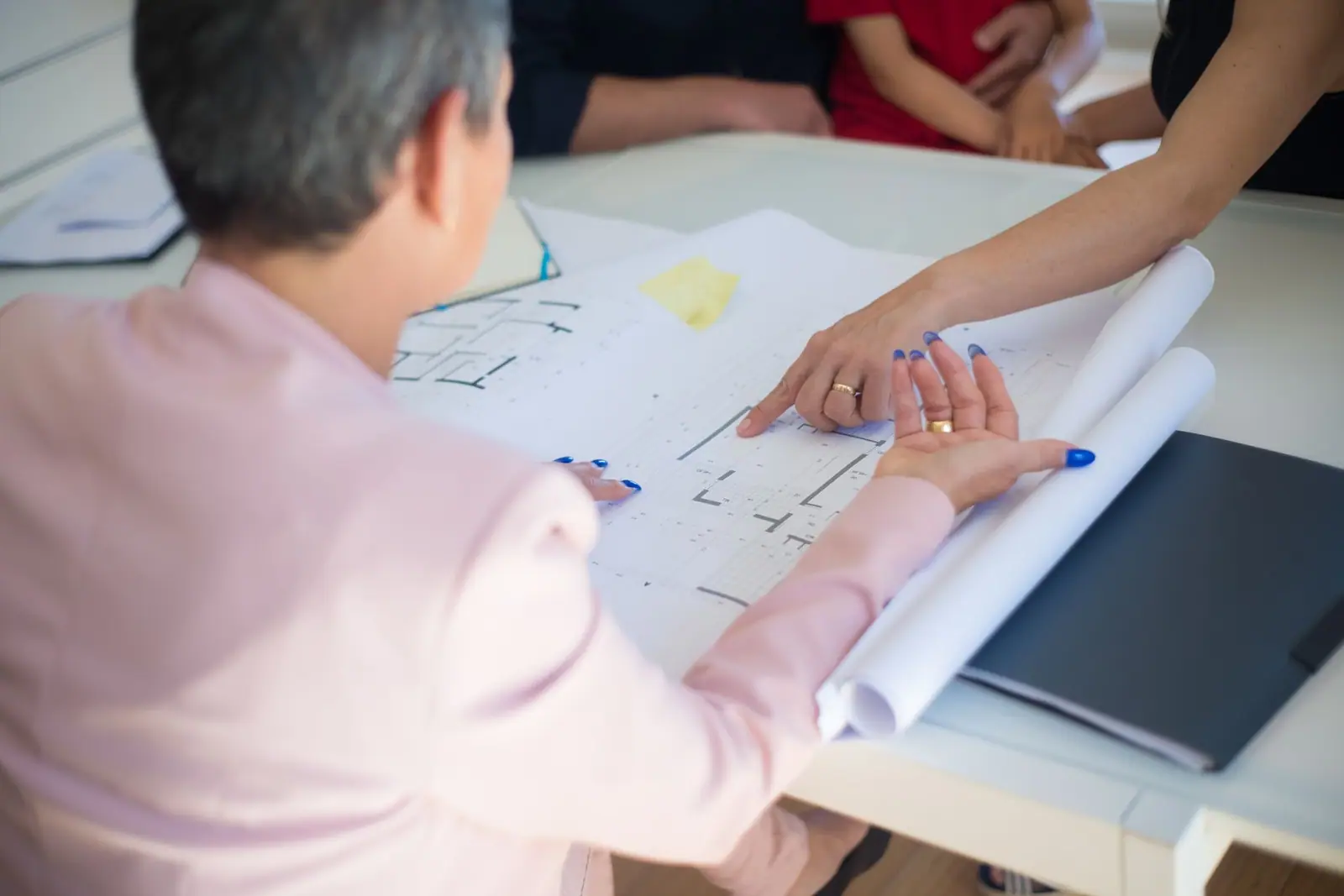 Several people pointing to drawings and papers spread across a table