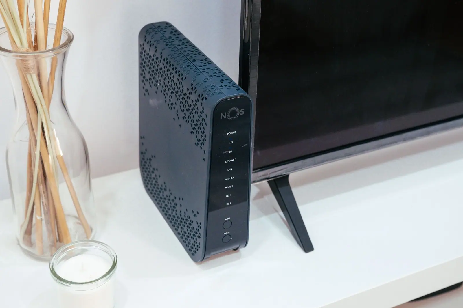An upright black NOS networking device on a white cabinet beside a television