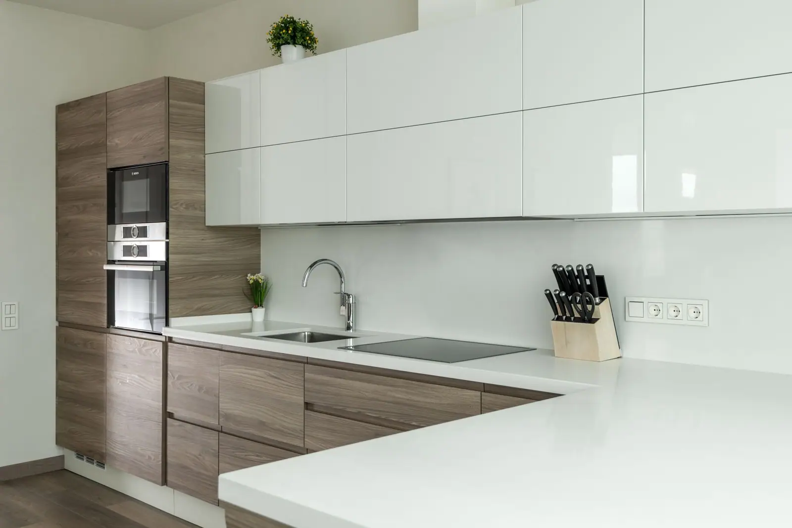 A modern kitchen with a sink, white glossy cabinets and wood-finish units
