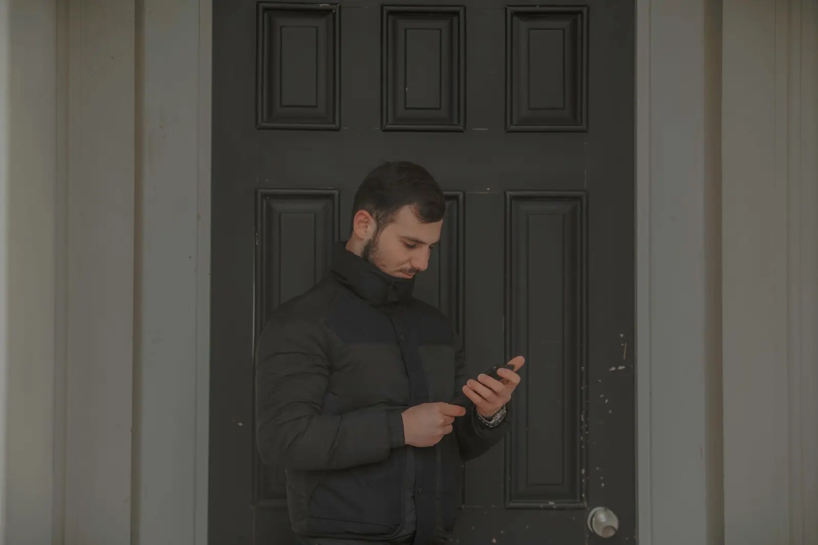 A man standing at a dark door looking at his phone
