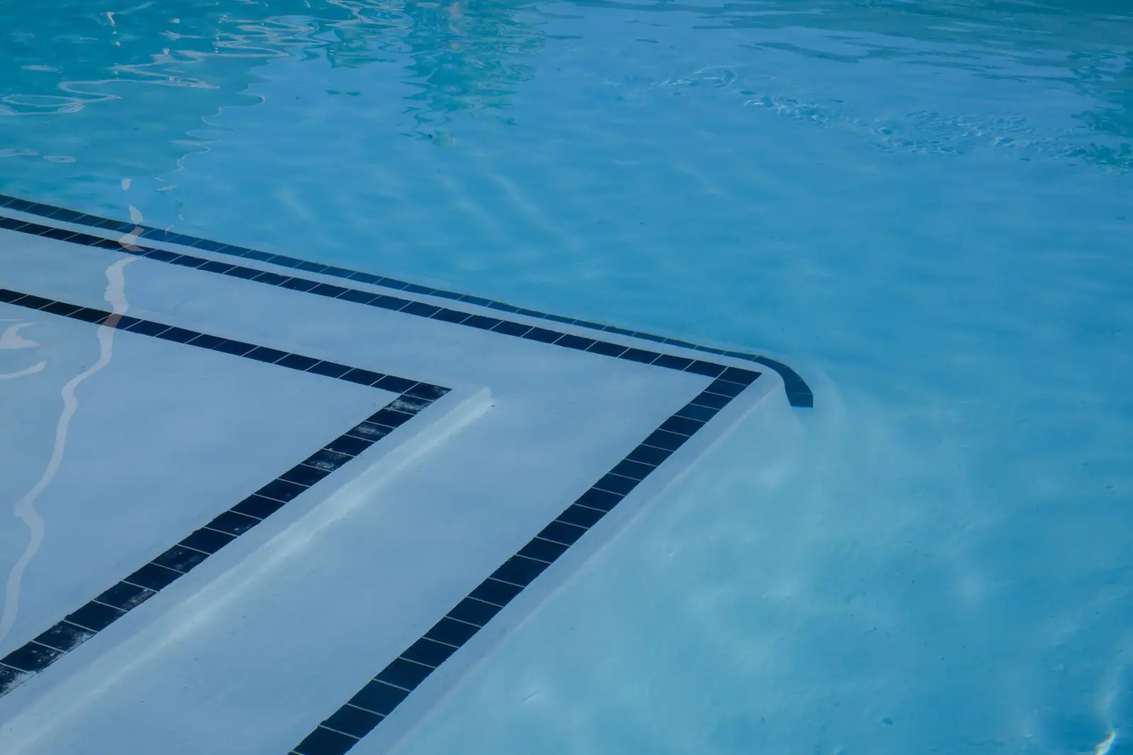 Clear blue pool water above light-colored submerged steps and a tiled pool edge