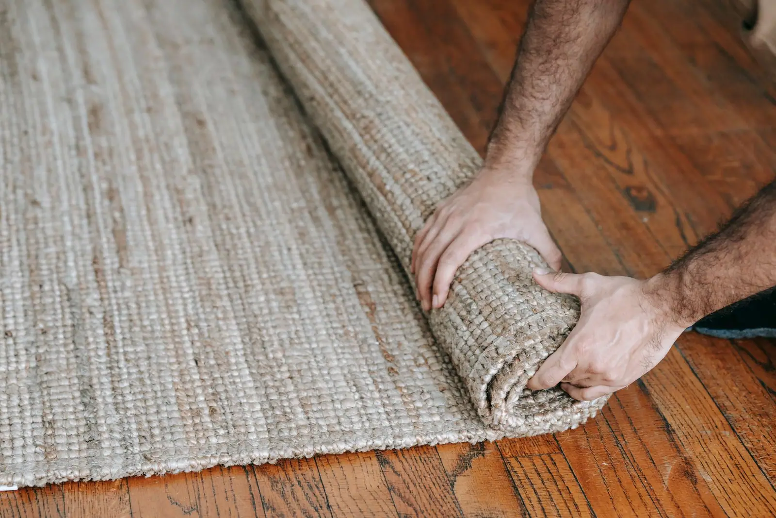 Hands rolling up a rug on a wooden floor