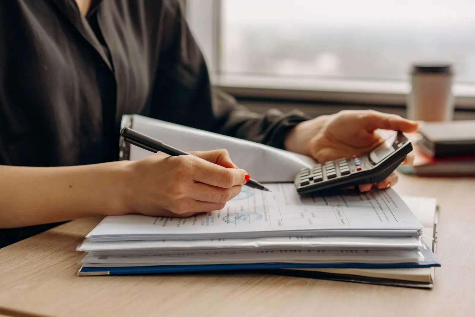 A hand writing on paperwork beside a calculator