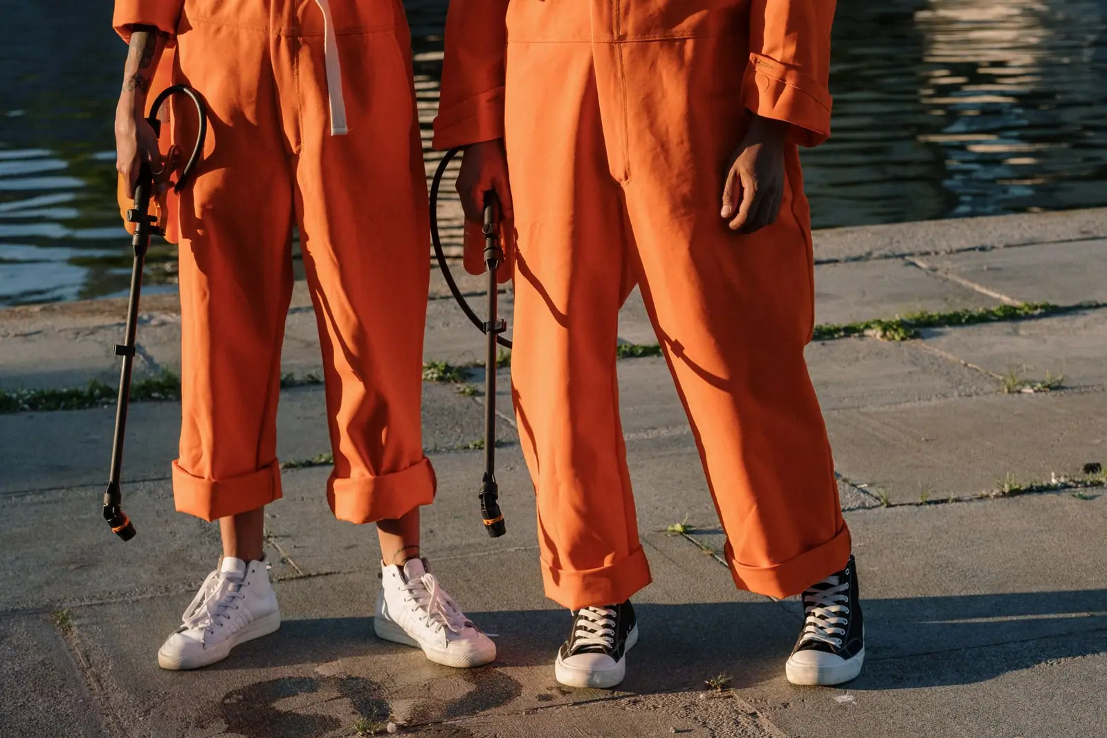 Two workers in orange jumpsuits holding sprayers on a concrete quay